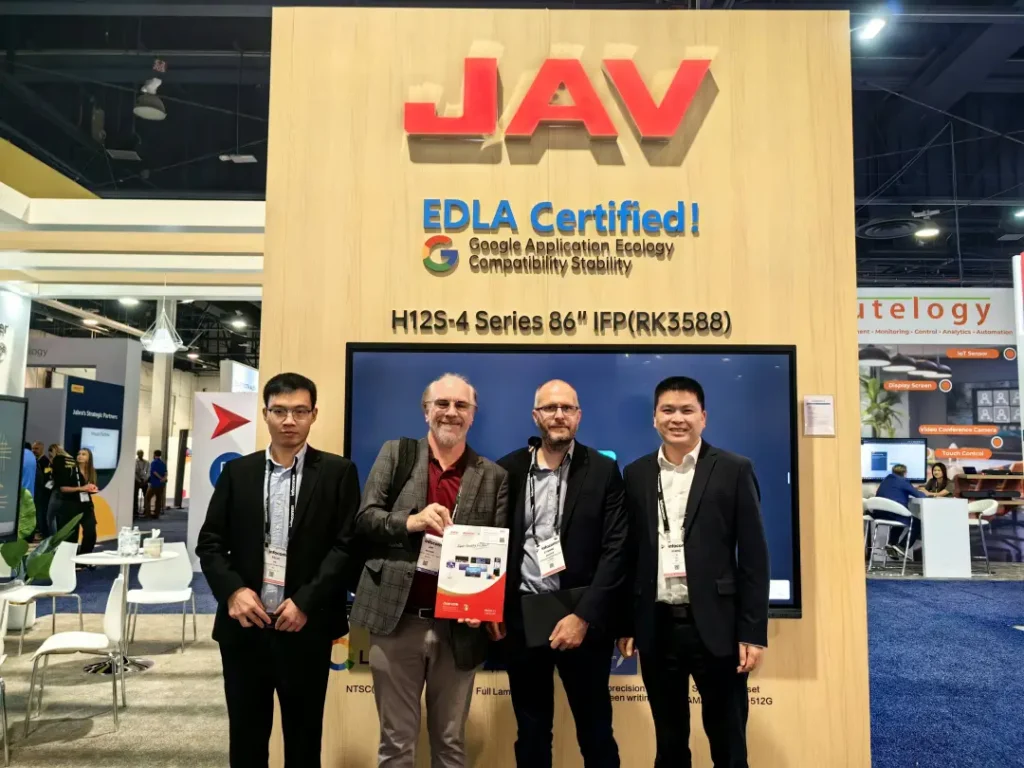 Four men standing in front of the JAV booth at a trade show, showcasing the EDLA Certified H12S-4 Series 86-inch Interactive Flat Panel Display.
